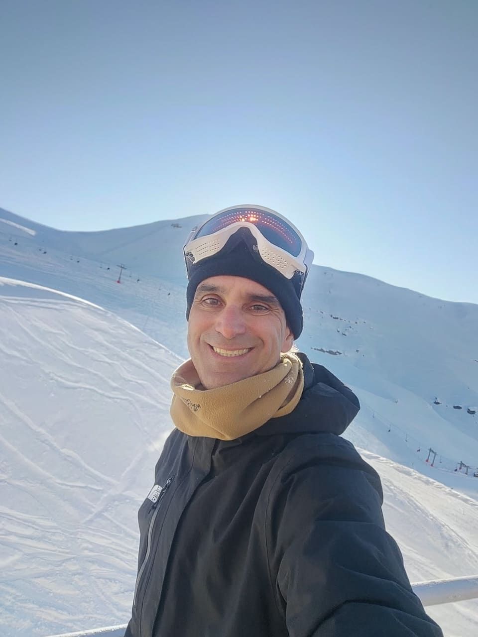 Selfie do Gustavo de gorro e óculos de esqui na testa, pistas brancas e teleféricos do Valle Nevado atrás